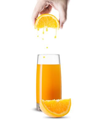 A hand is squeezing an orange into a glass of orange juice.