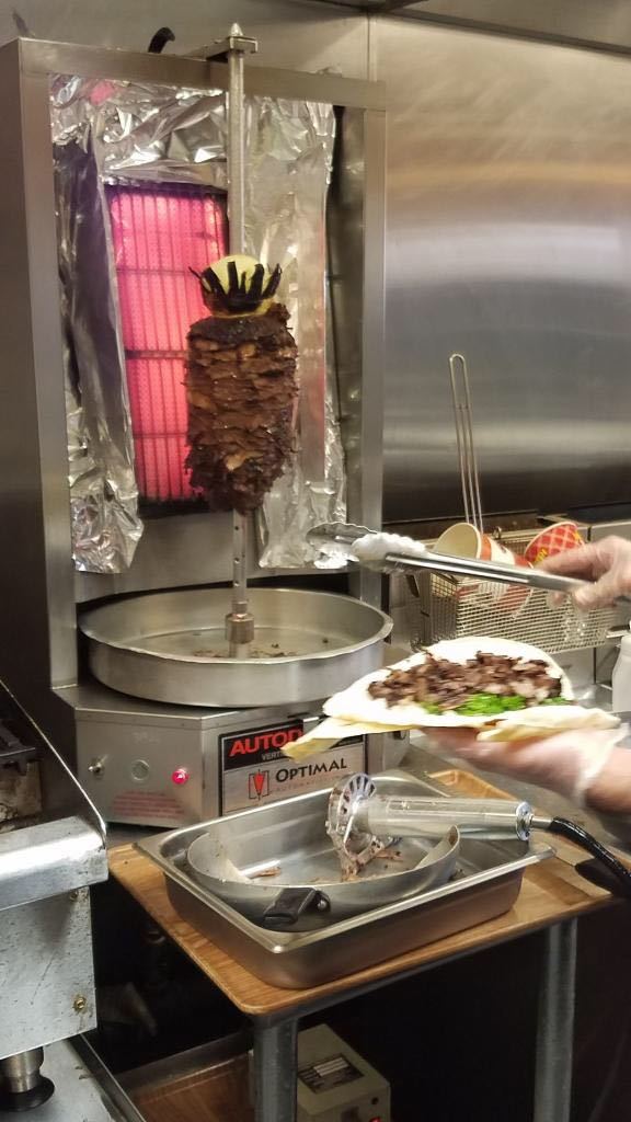 A person is holding a plate of food in front of a shawarma machine