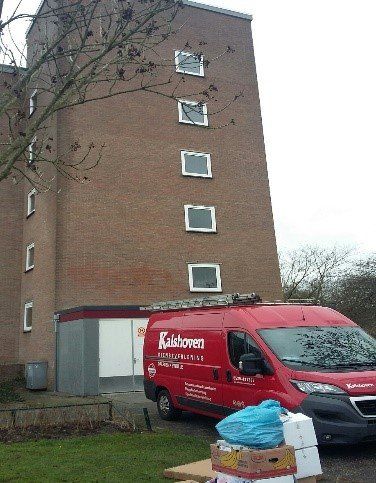 Een rode bestelwagen staat geparkeerd voor een hoog bakstenen gebouw