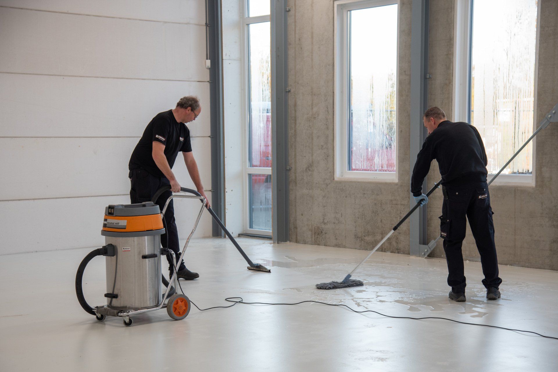 Twee mannen maken de vloer van een gebouw schoon met stofzuigers.