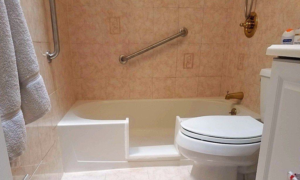 Bathroom with a step-in tub-shower combo, beige tile, grab bar, and a toilet in the foreground