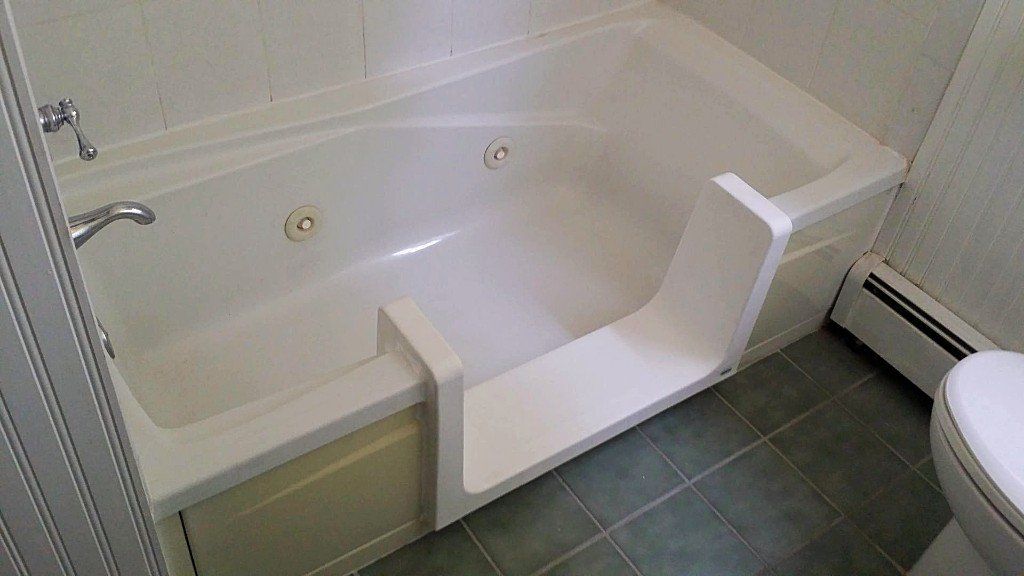 Accessible step-in bathtub with a built-in seat in a tiled bathroom.