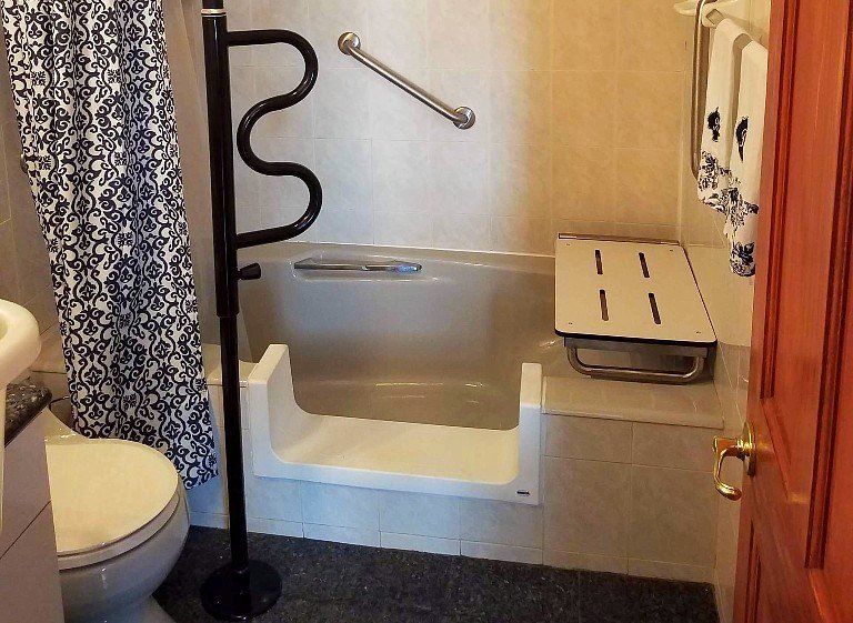 Bathroom with step-in accessible tub, grab bar, bench seat, and shower curtain.
