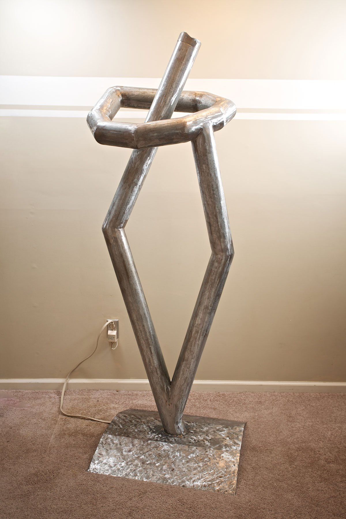 A large metal sculpture is sitting on a carpeted floor in a room.