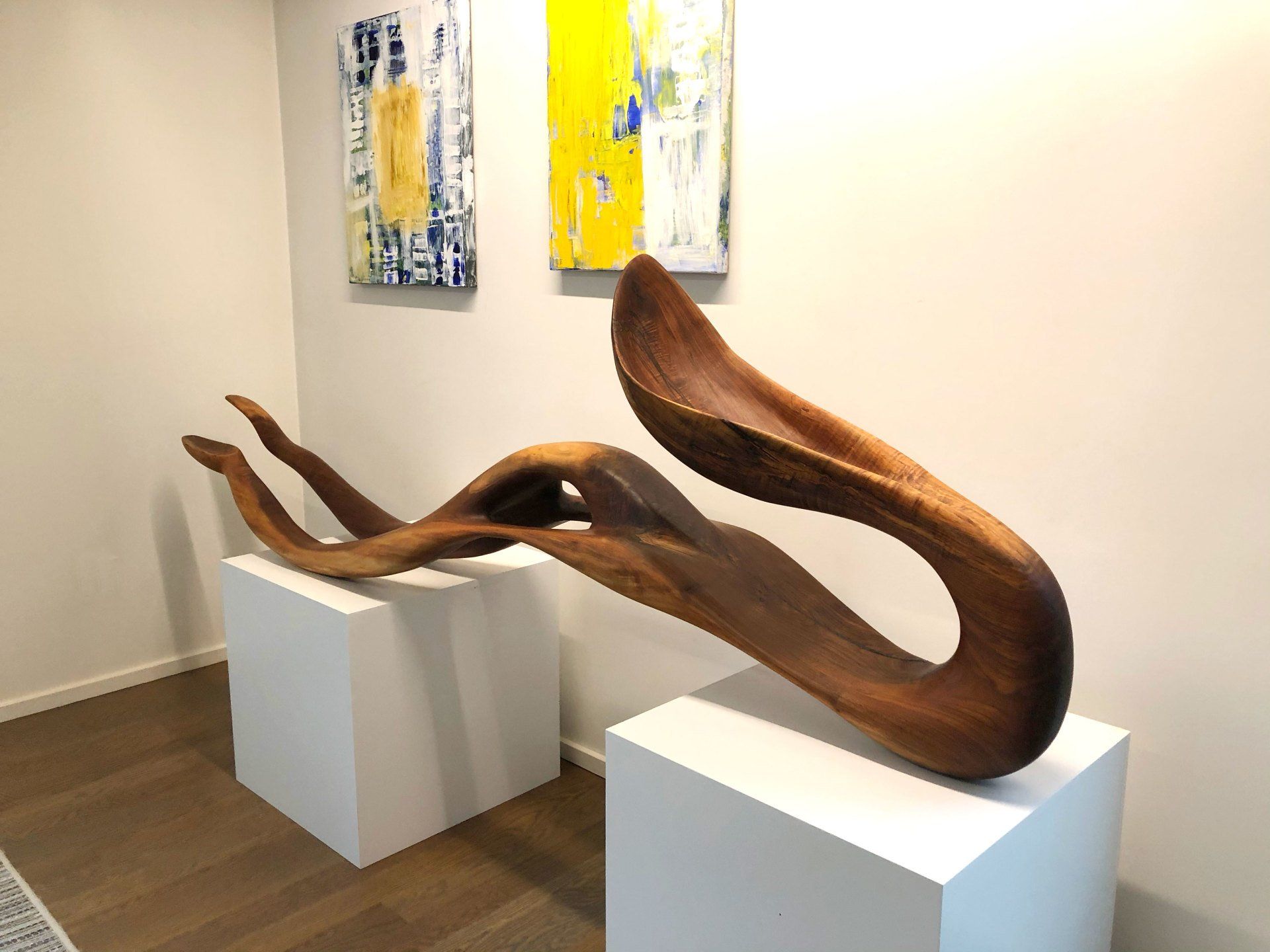 A large wooden sculpture is sitting on a white pedestal in a room.
