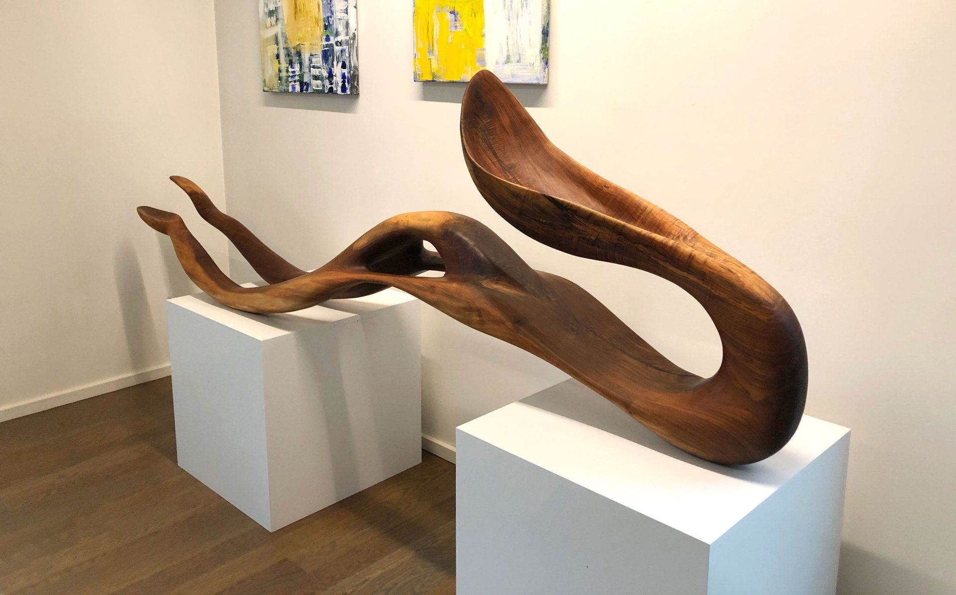 A large wooden sculpture is sitting on a white pedestal in a room.