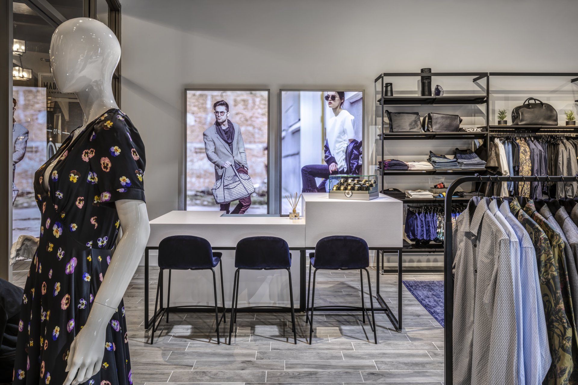 A mannequin is standing in a clothing store next to a table and chairs.