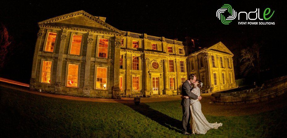 A bride and groom are kissing in front of a large building at night.