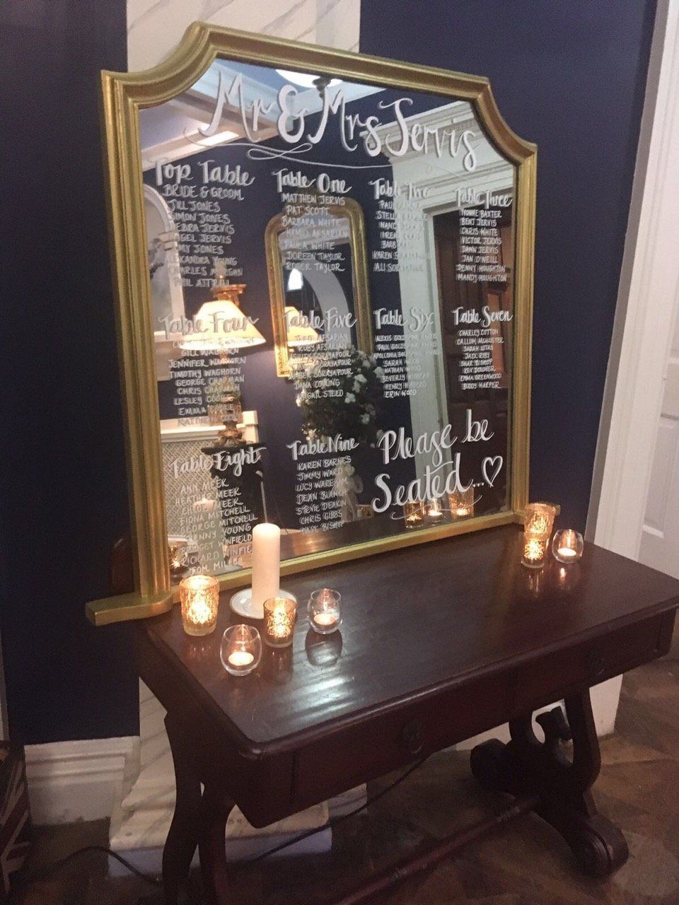 A table with candles and a mirror that says please be seated