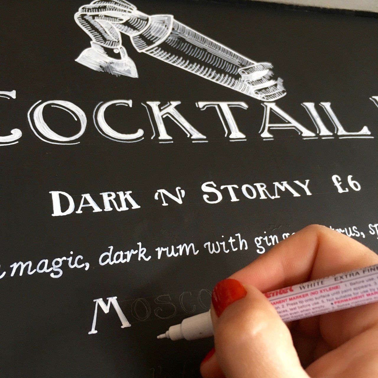 A person is writing on a blackboard that says cocktail dark n stormy