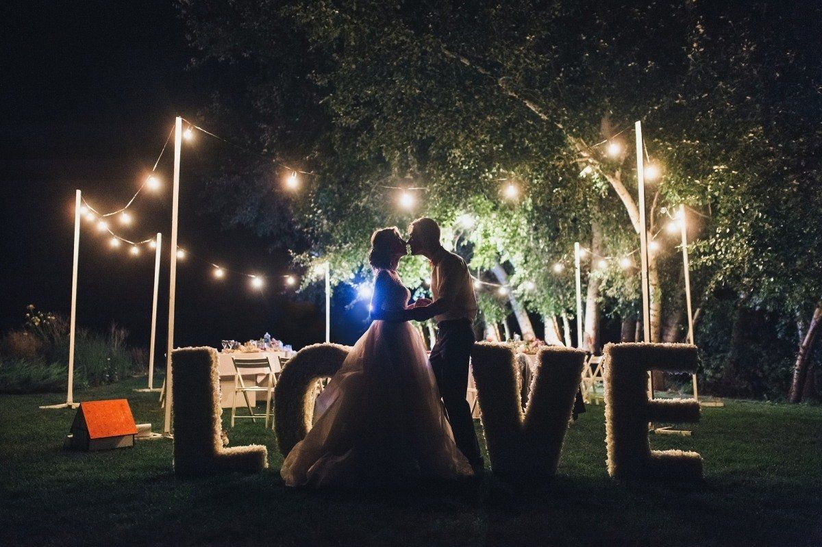 A bride and groom are kissing in front of a large love sign.