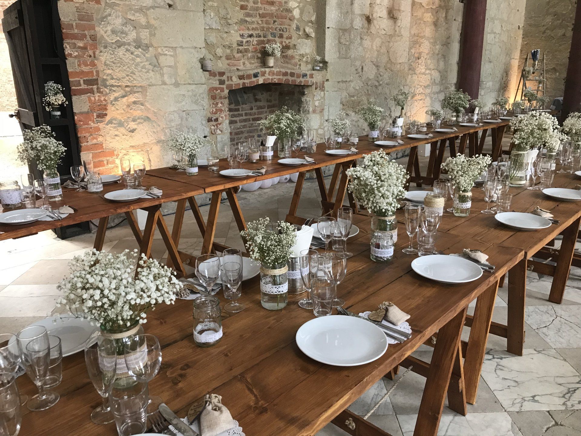 A long wooden table with plates , glasses , and vases of baby 's breath on it.