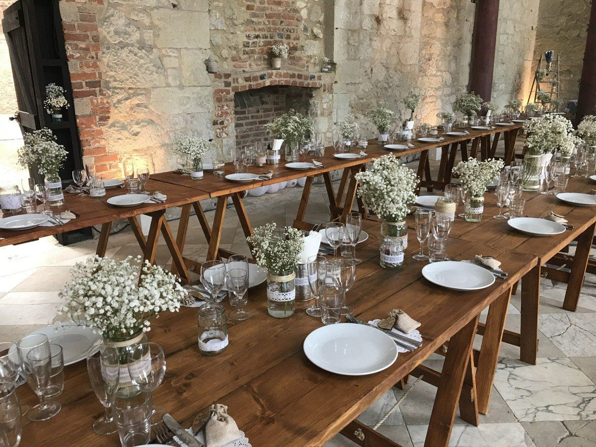 A long wooden table with plates , glasses , and vases of baby 's breath on it.