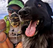 Person with a green visor and sunglasses smiles next to a panting black dog.