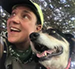 Person smiling with dog, both looking up and to the left. Person wears a green cap and bandana.