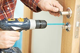 A man is using a drill to fix a door handle.