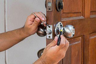 A man is fixing a door knob with a screwdriver.