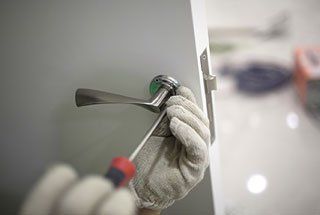 A person is fixing a door handle with a screwdriver.