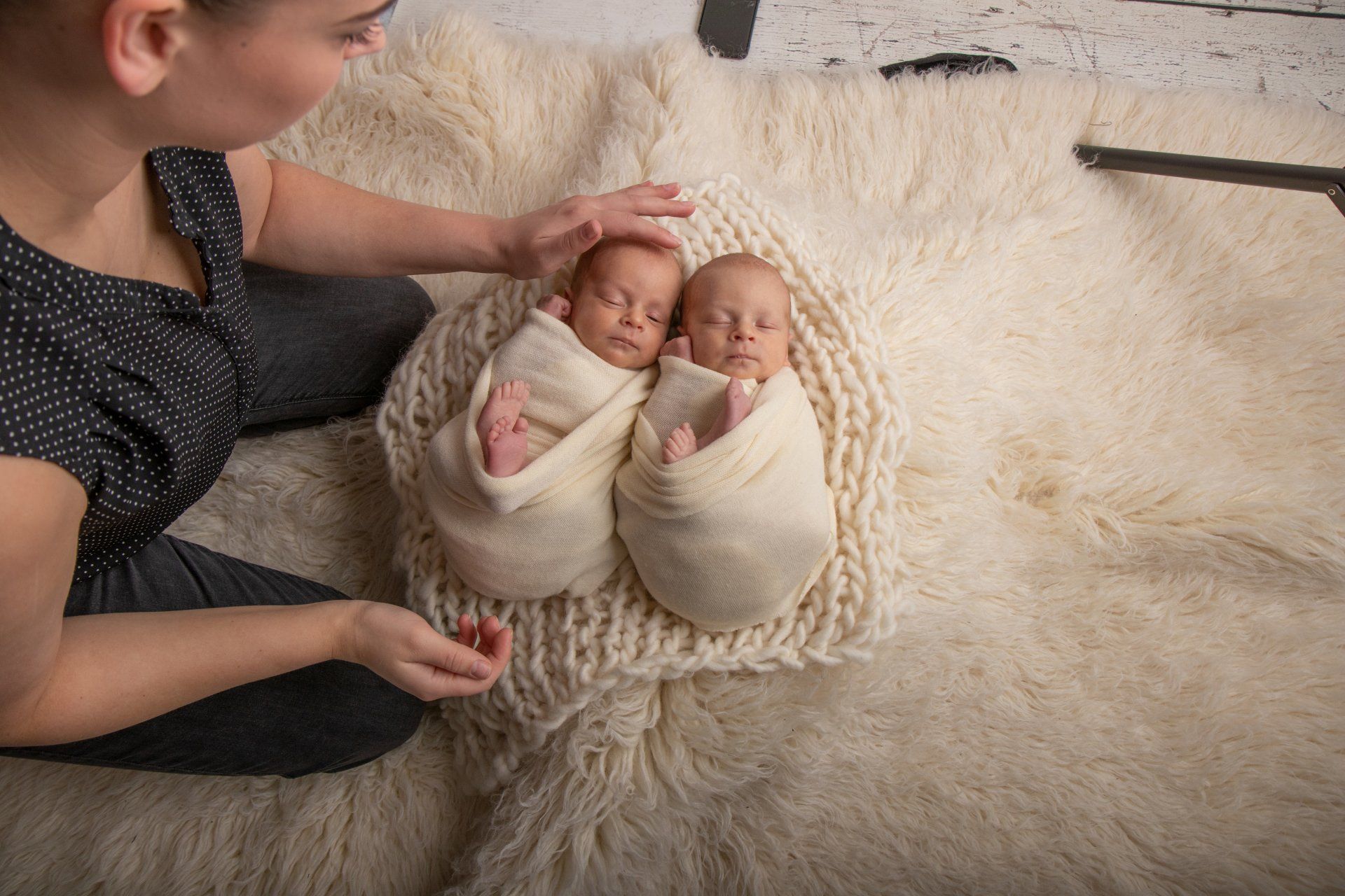 Een vrouw streelt voorzichtig twee ingewikkelde pasgeboren baby's die op een zachte, crèmekleurige deken liggen.