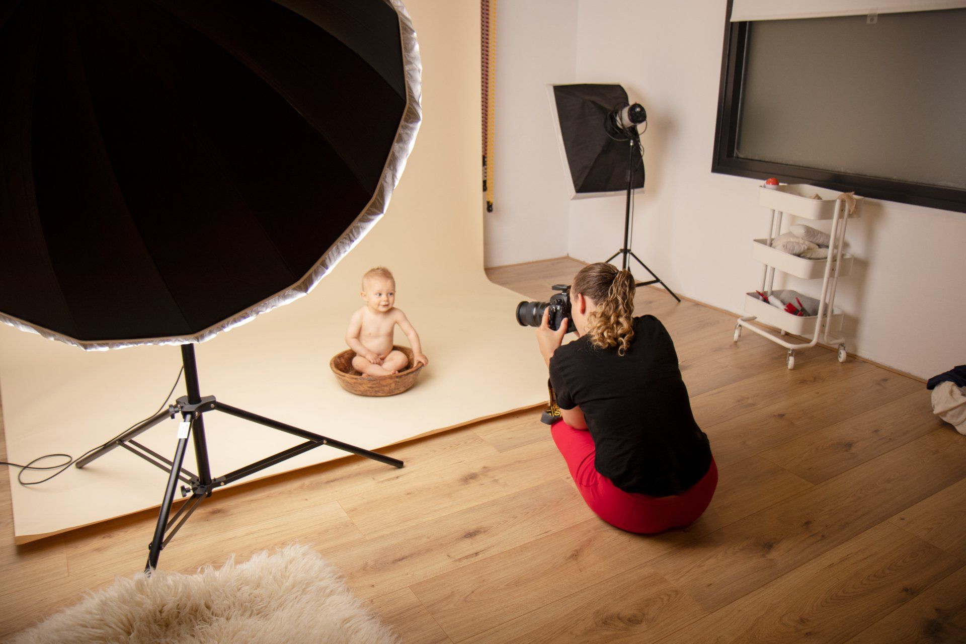 Baby poseert in een studio met een fotograaf, een grote lichtkoepel en een achtergrond.