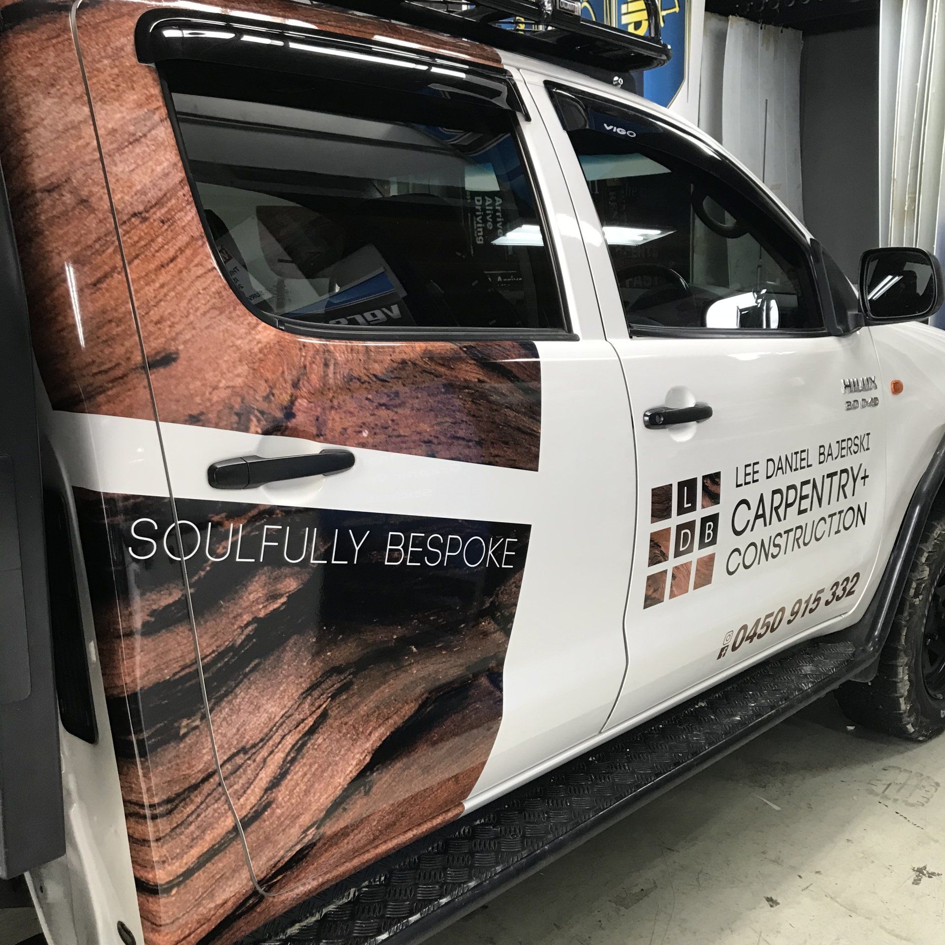 White pickup truck with wood-grain wrap and “Carpentry Construction” logo on the side