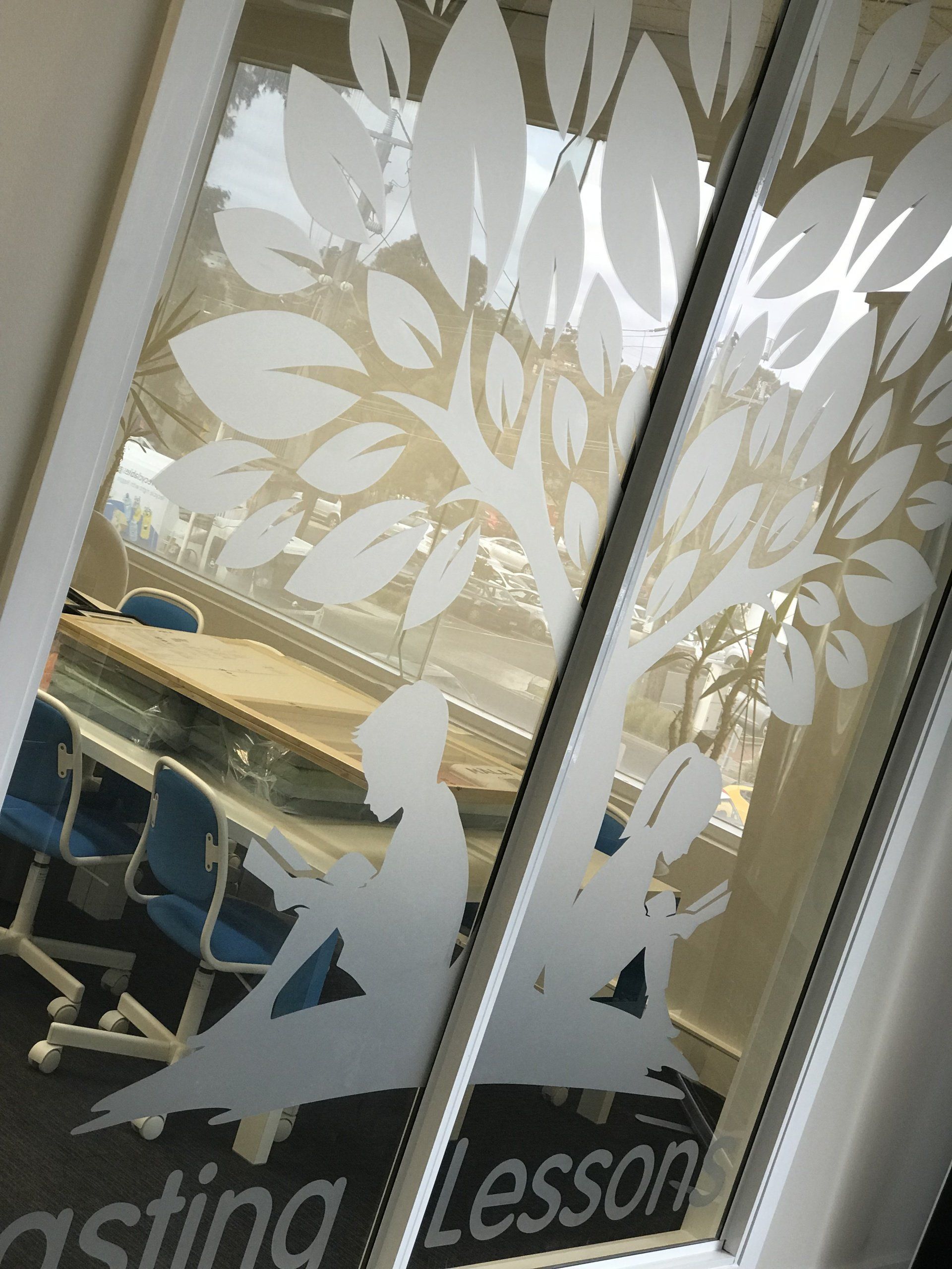 Frosted window with tree design. Silhouette of figures reading under tree. 
