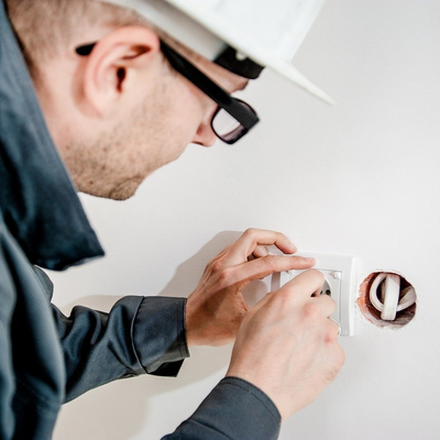 a man wearing a hard hat and glasses working on an electrical outlet