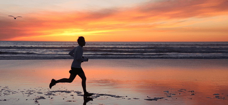 A woman is running on the beach at sunset.