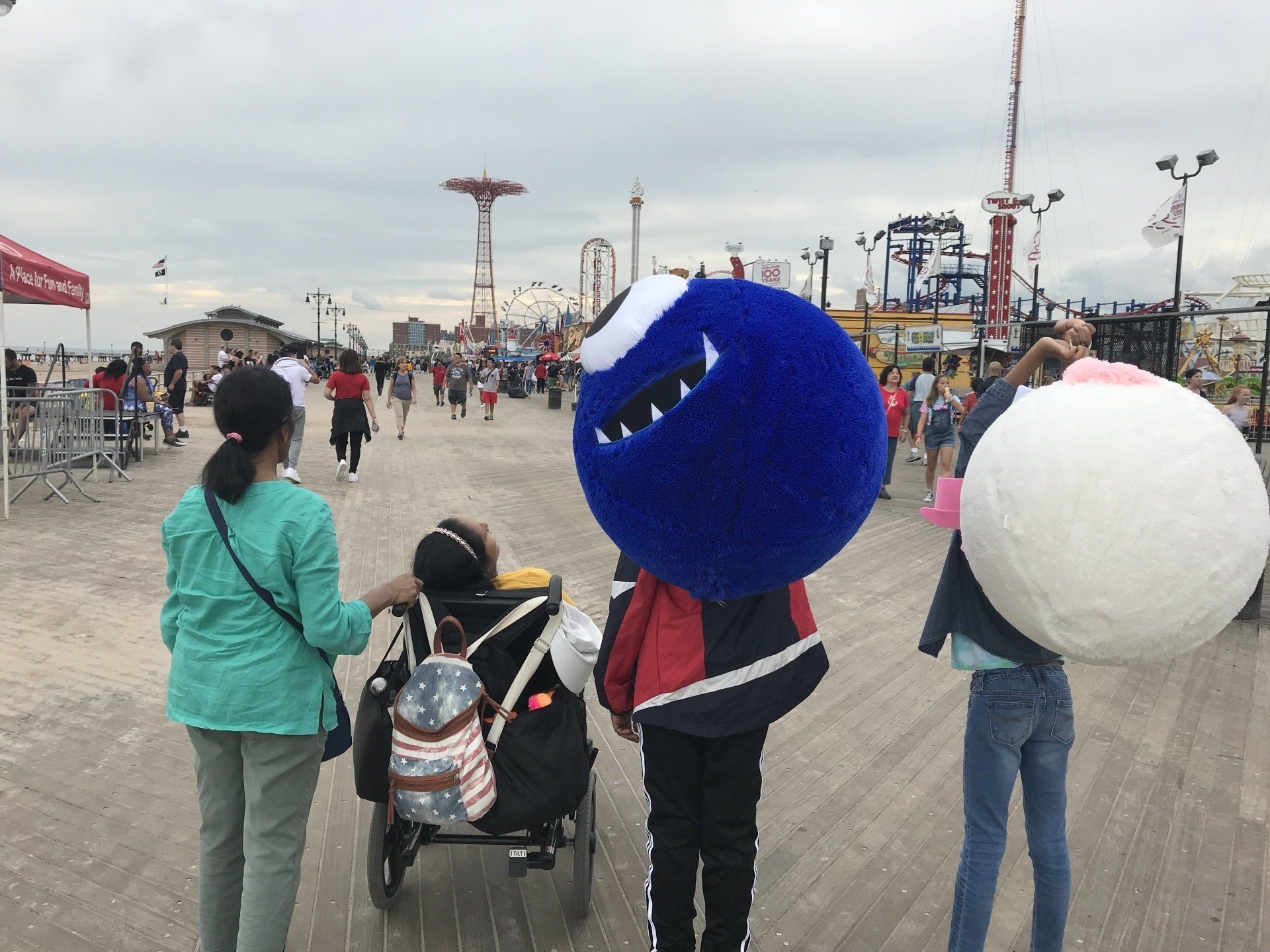 It's  gloomy day with many people on the Boardwalk. There is a large ride in the forefront and our family looking at them. 