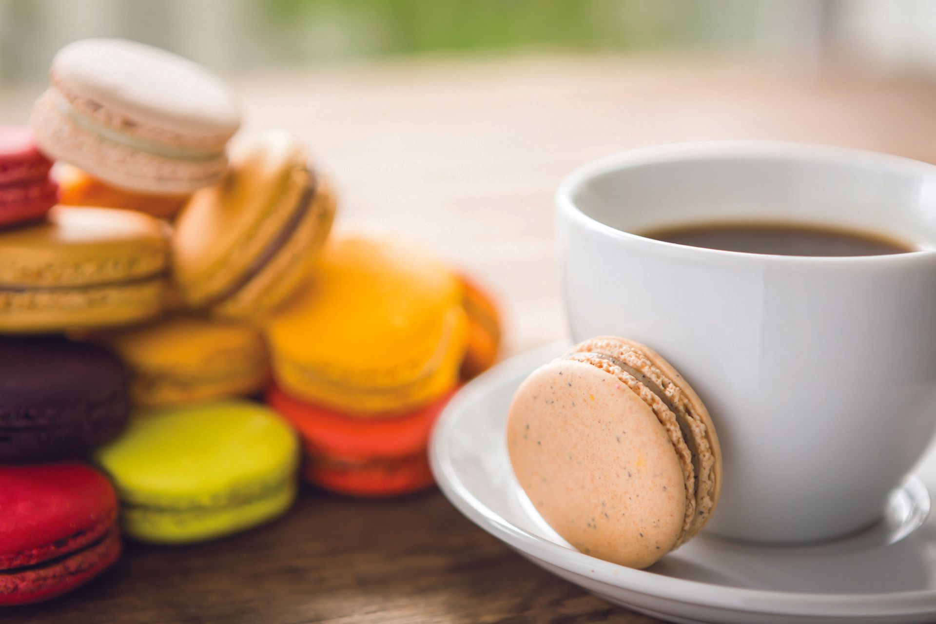 Coffee served with colourful macarons on a table in natural light