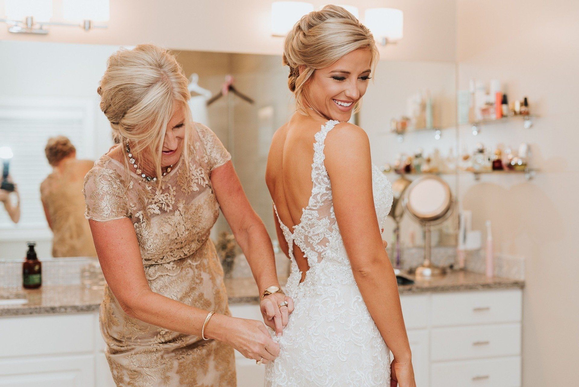 A woman is helping a bride get ready for her wedding in a bathroom.