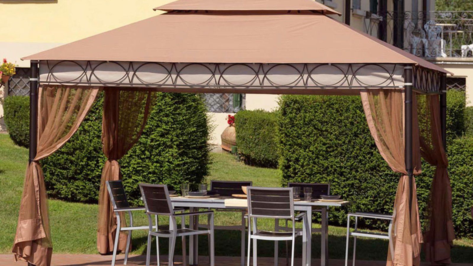 Pergola di giardino di colore marrone con zanzariere  avvolgibili, tavolo e sedie di metallo e legno