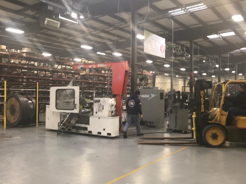 Factory floor with machinery, a worker, and a forklift in a warehouse aisle