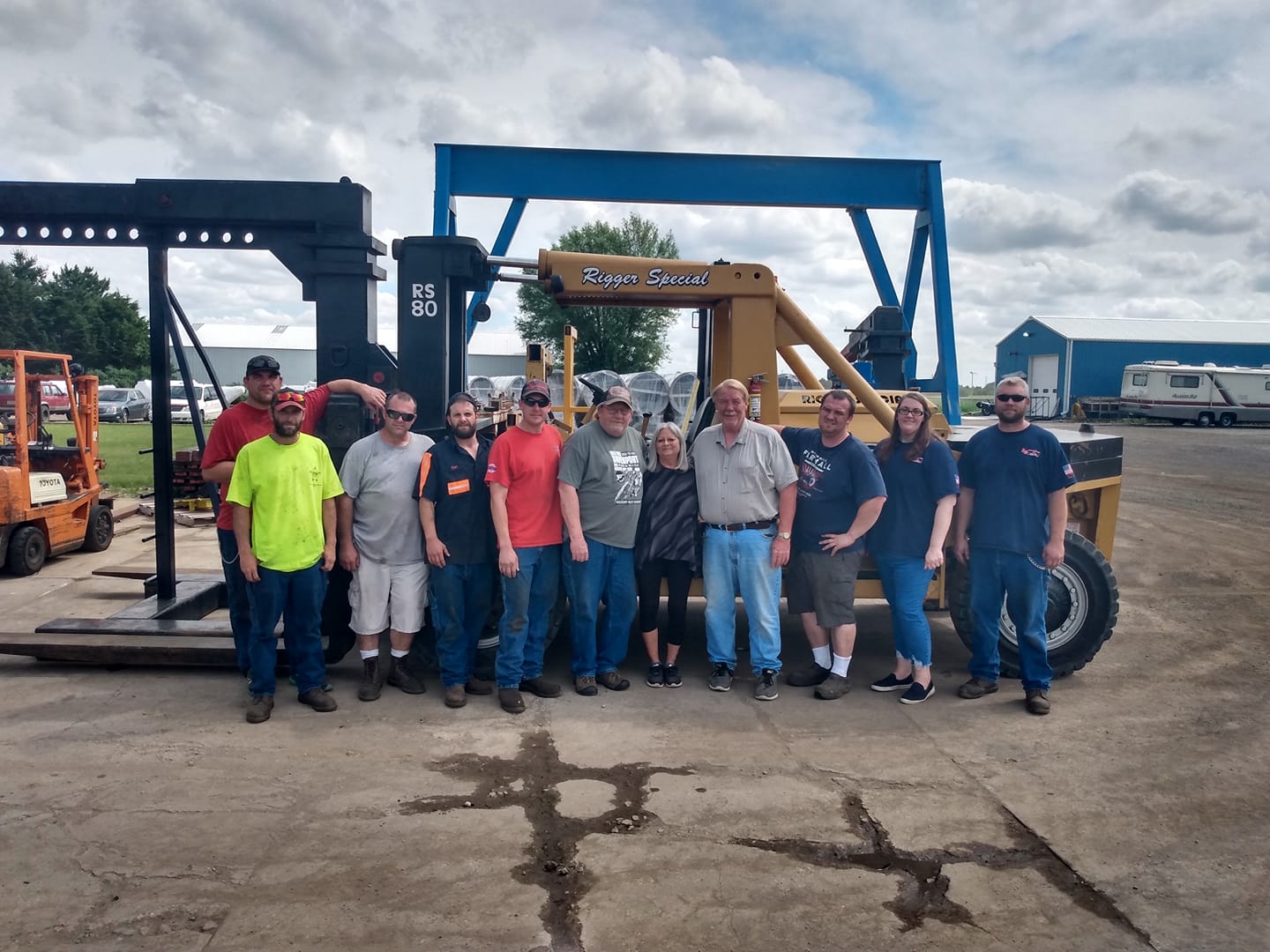 Group of people standing in front of a blue construction lift in an outdoor equipment yard
