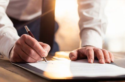 Hands signing a document on a desk in warm light