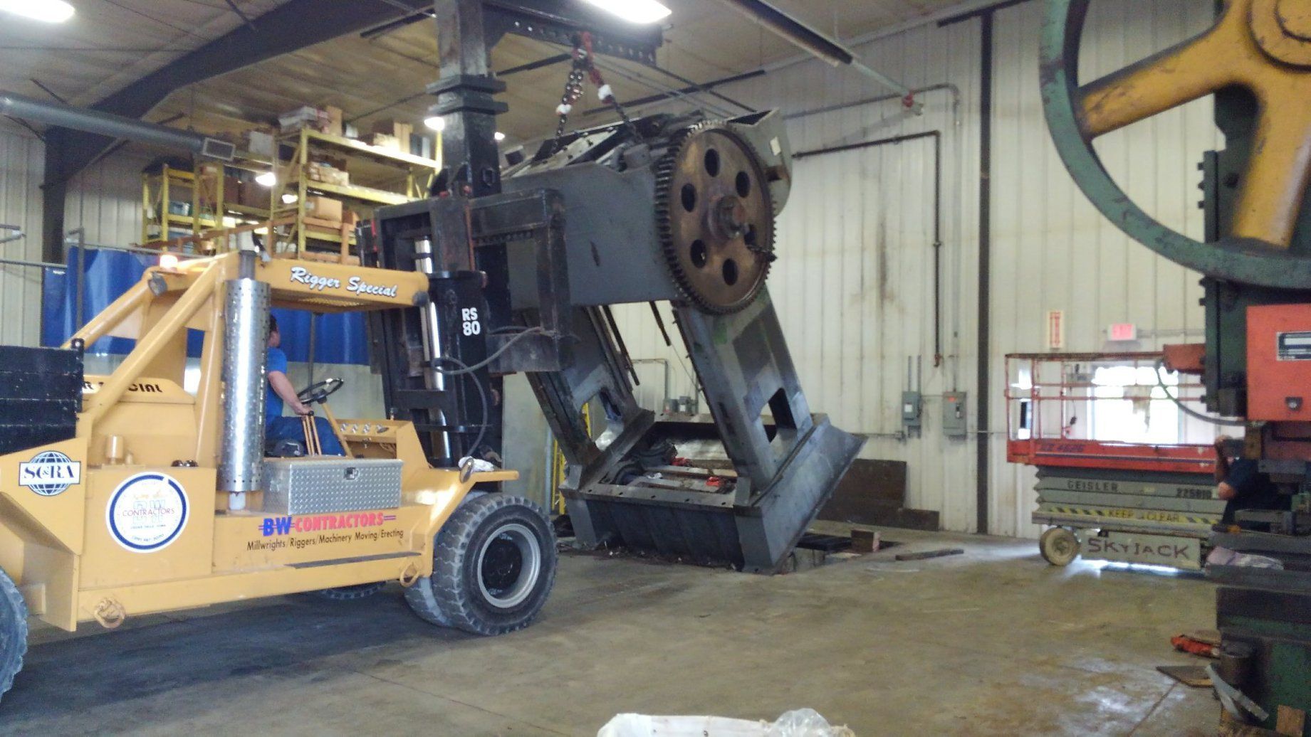 Yellow forklift lifting a large black industrial machine inside a warehouse workshop