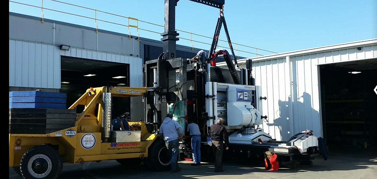 Crane Lifting — Cedar Falls, IA — BW Contractors Inc. Workers using a yellow forklift to load heavy equipment onto a truck outside a warehouse