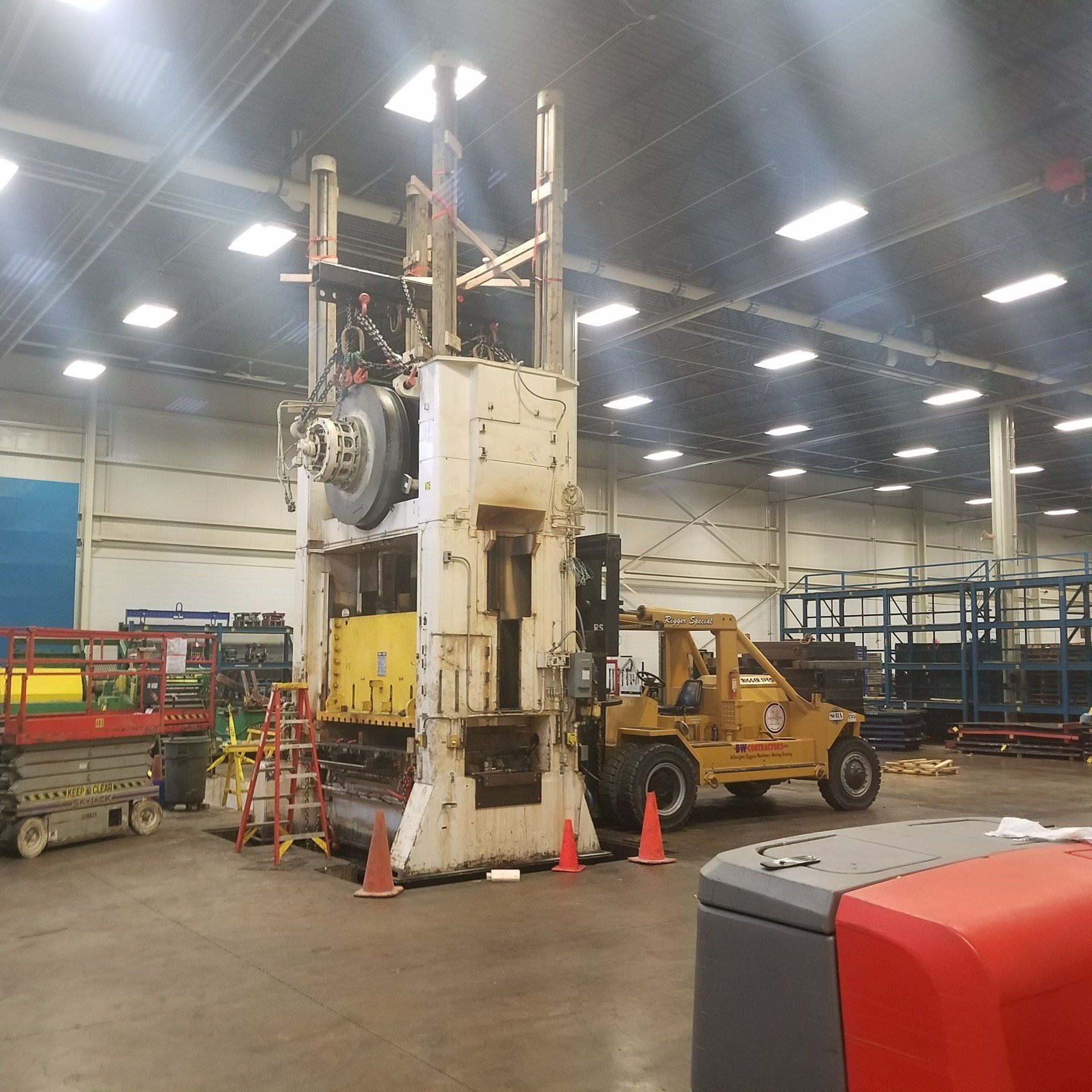 Large industrial machine in a warehouse, surrounded by cones and a forklift.