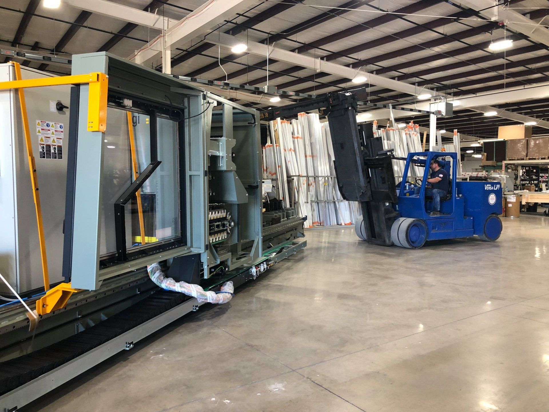 Blue forklift moving large industrial equipment inside a warehouse with overhead lighting.
