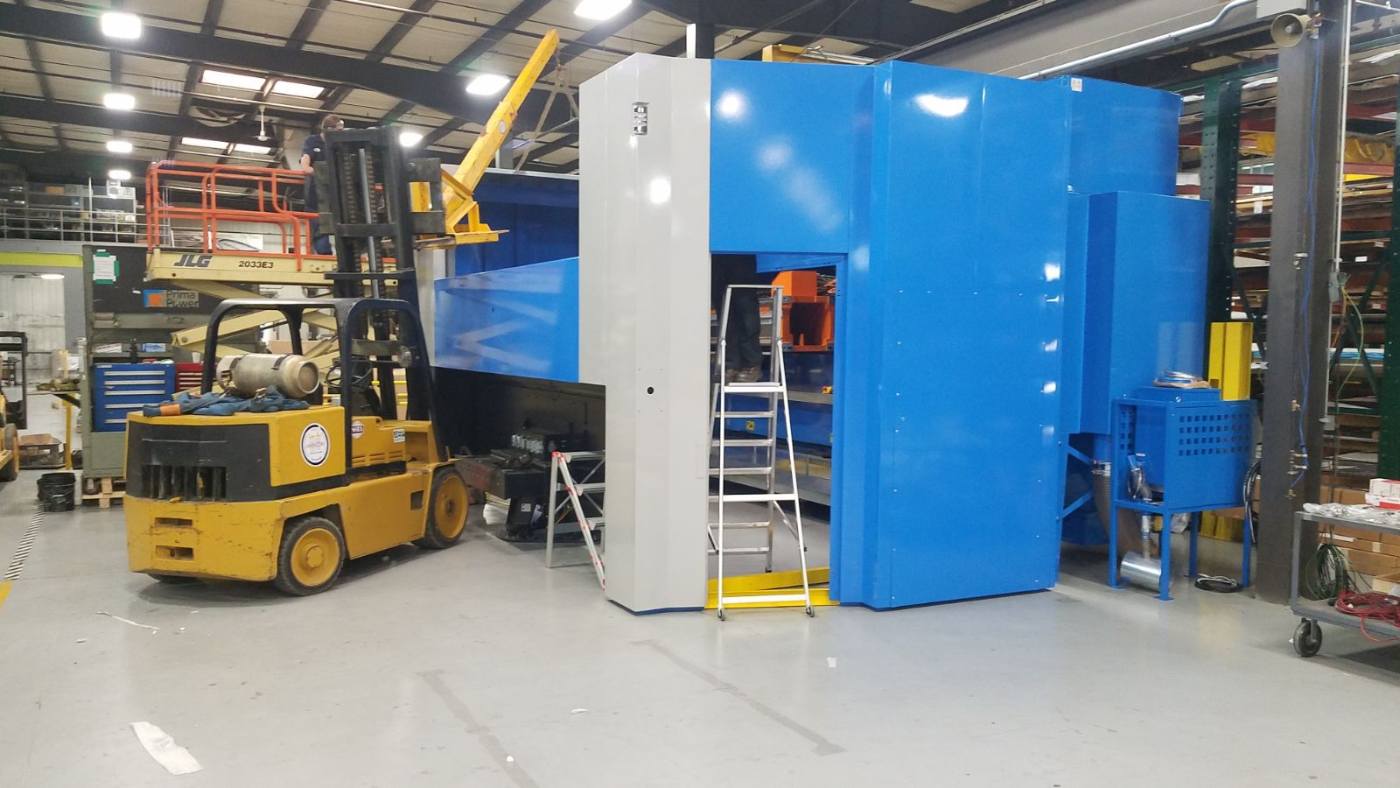 Yellow forklift beside large blue industrial machine in a warehouse factory floor