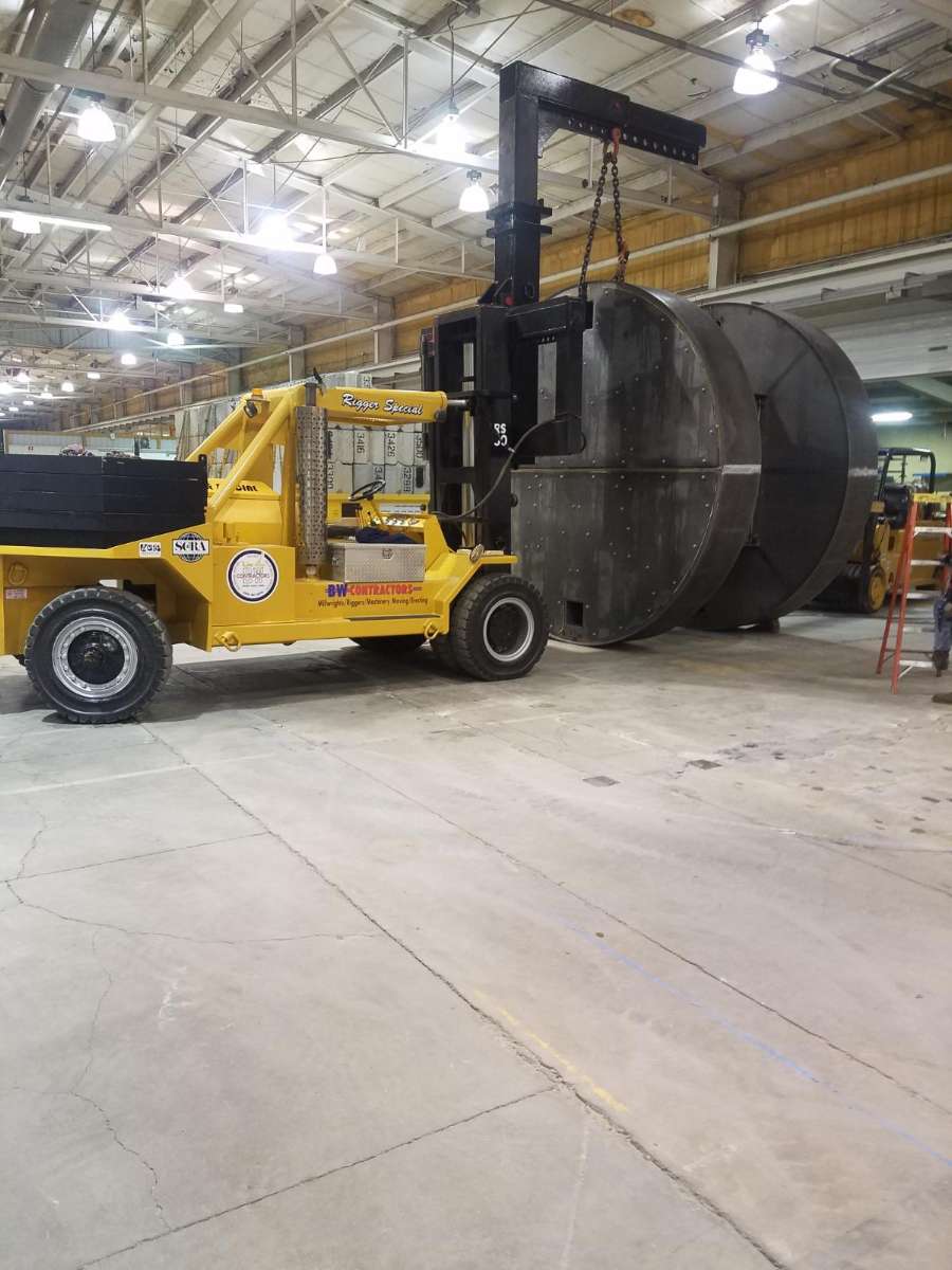 Yellow forklift lifting a huge black cylindrical tank in an industrial warehouse