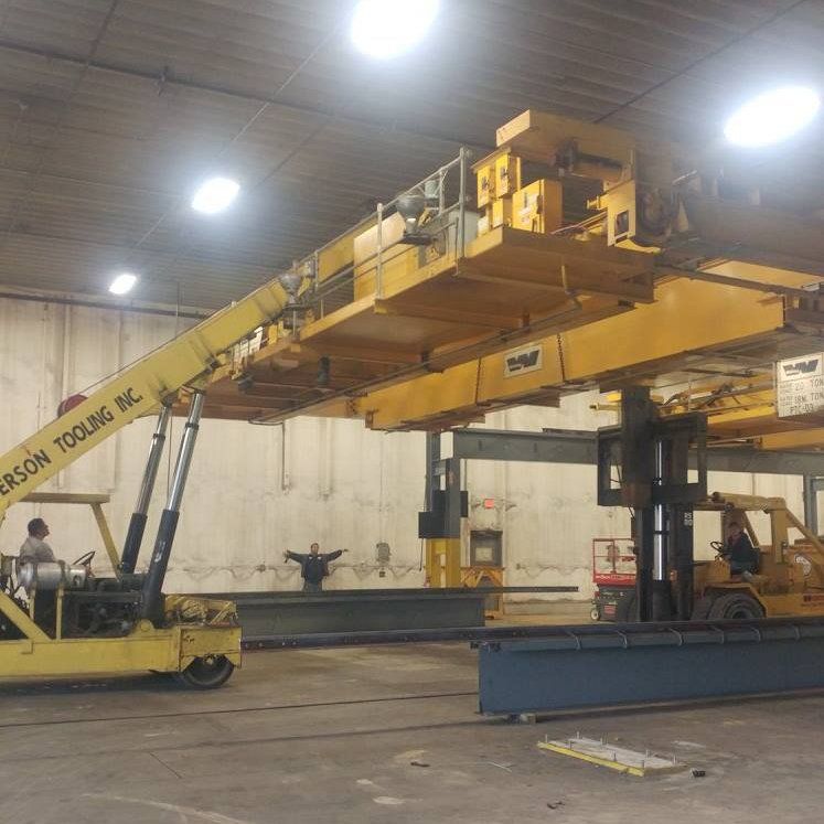 Yellow aerial lift raising a large orange overhead structure inside an industrial warehouse