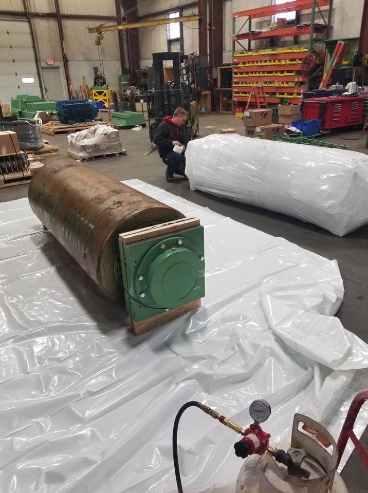 Warehouse with a person kneeling by wrapped industrial equipment on a plastic-covered floor