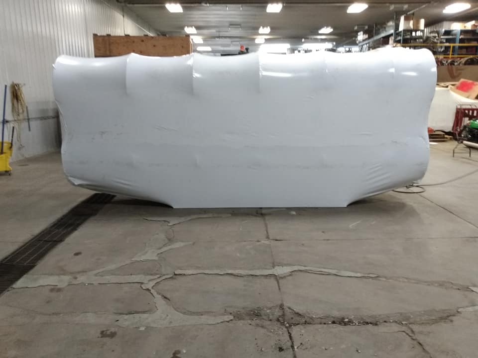 Large white industrial tank or molded container in a warehouse workshop, centered on a concrete floor.