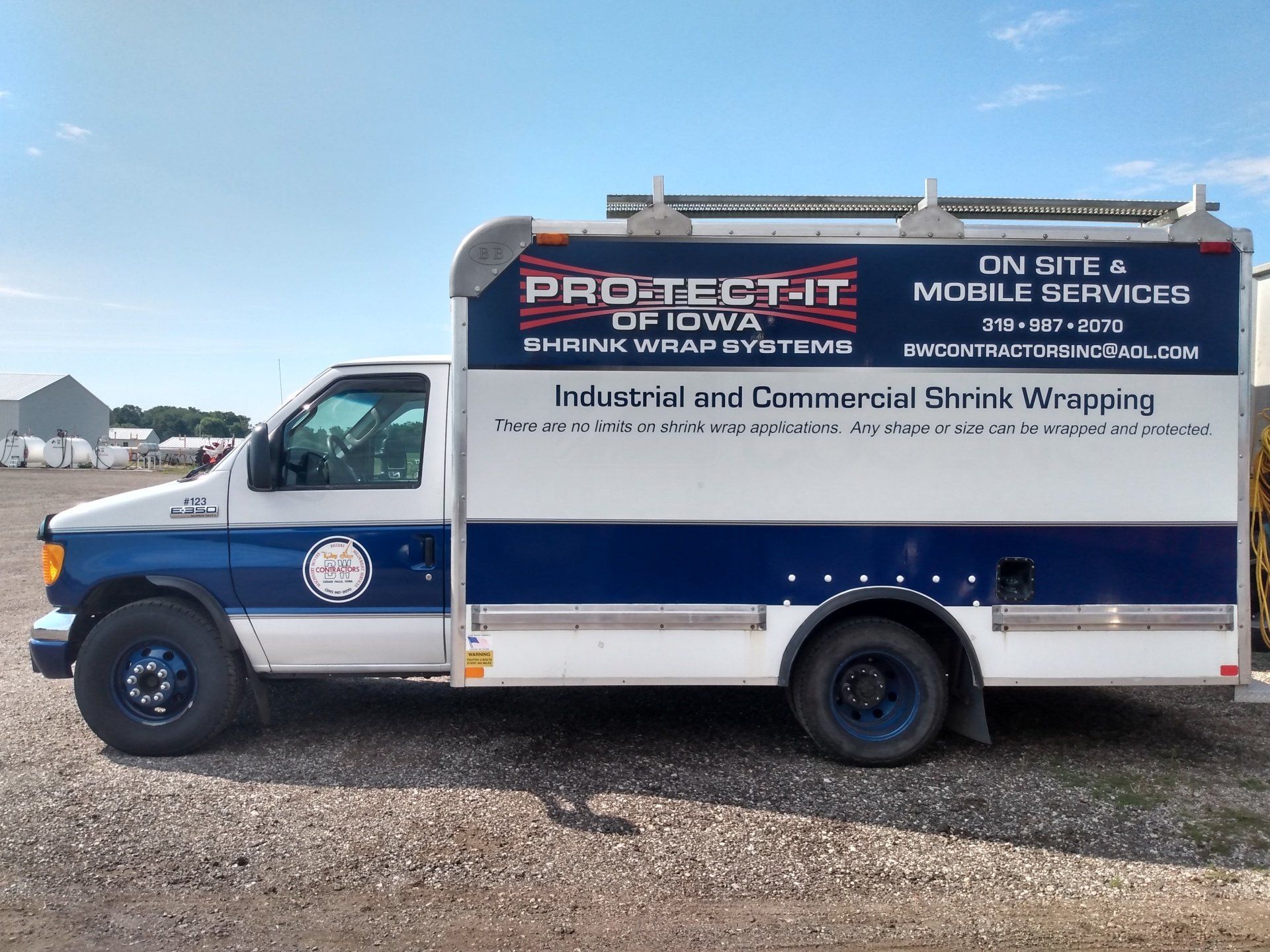 White service truck with blue stripe and roofing company signage parked on gravel under a blue sky