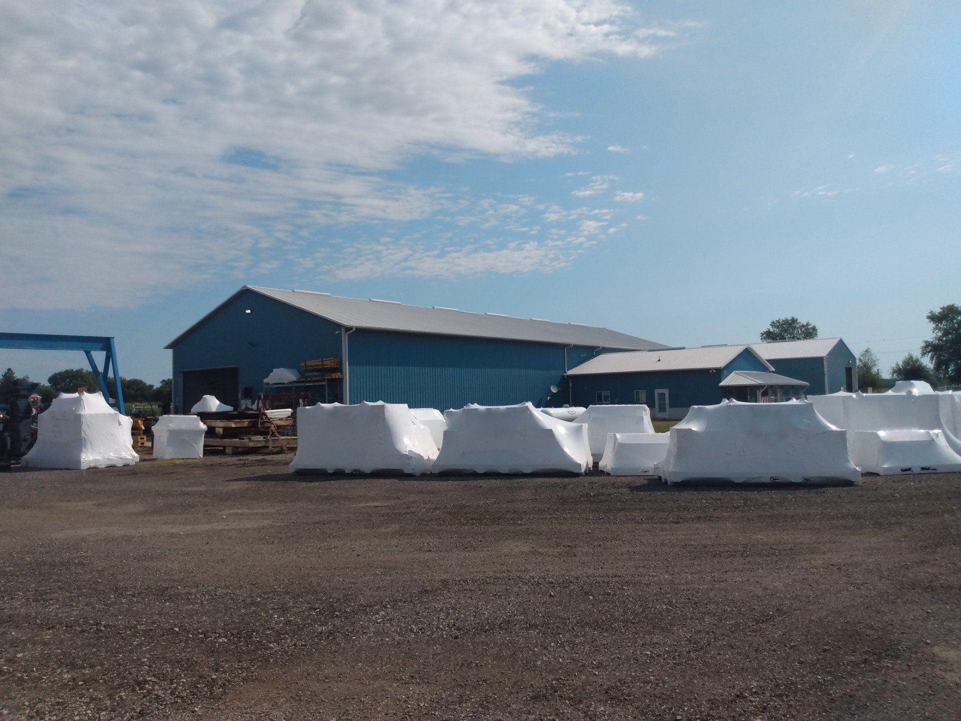 Large white-wrapped hay bales stacked in a farm yard beside a blue barn under a cloudy sky