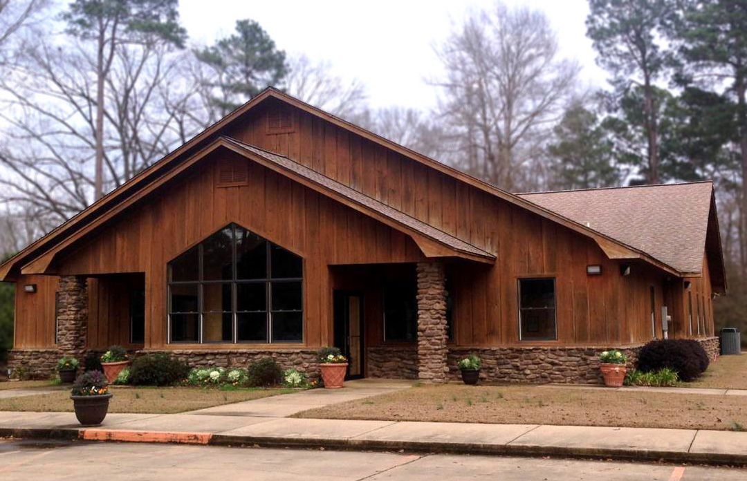 Wooden cabin-style building with a stone base and large windows, surrounded by trees on a cloudy day