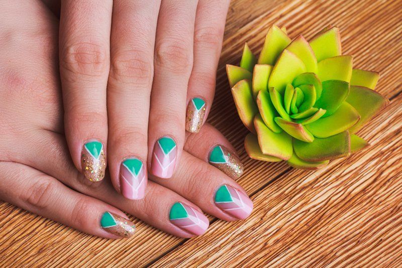 Mani con nail art geometrica accanto a una succulenta verde su legno.