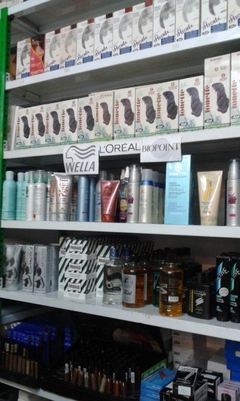 Scaffali pieni di tinture per capelli, shampoo e prodotti per lo styling in un negozio. Tra i marchi presenti figurano Wella e L'Oréal.