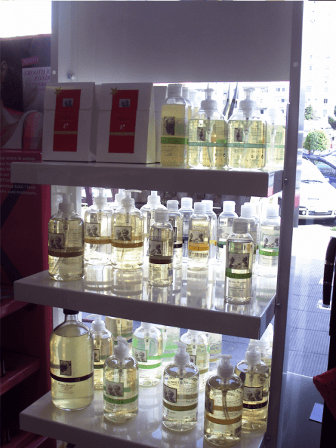 La scaffalatura espone bottiglie di prodotti liquidi con etichette bianche e verdi, illuminate da luci soffuse.